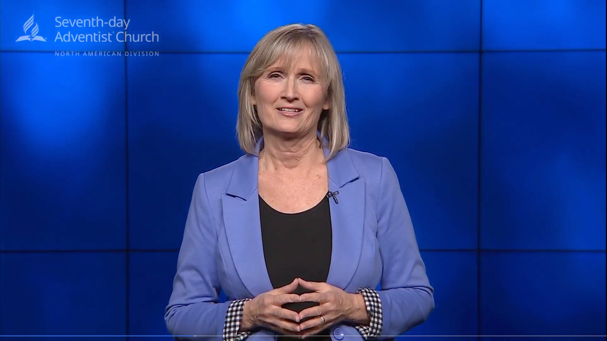 Smiling white woman standing in front of a blue screen in a video report. 