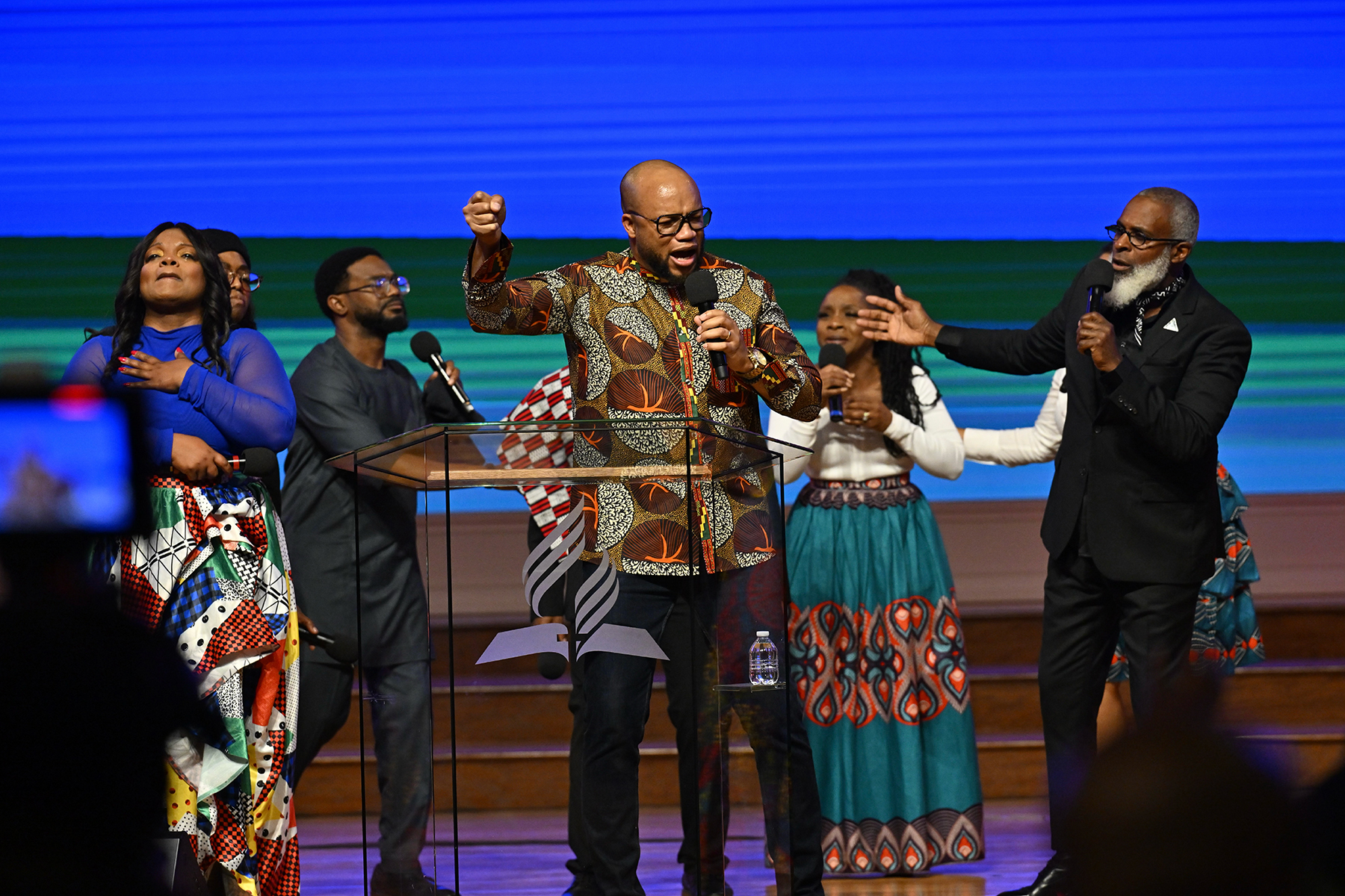 A Black praise and worship team on stage, wearing African outfits and singing passionately. The leader is in the middle. 