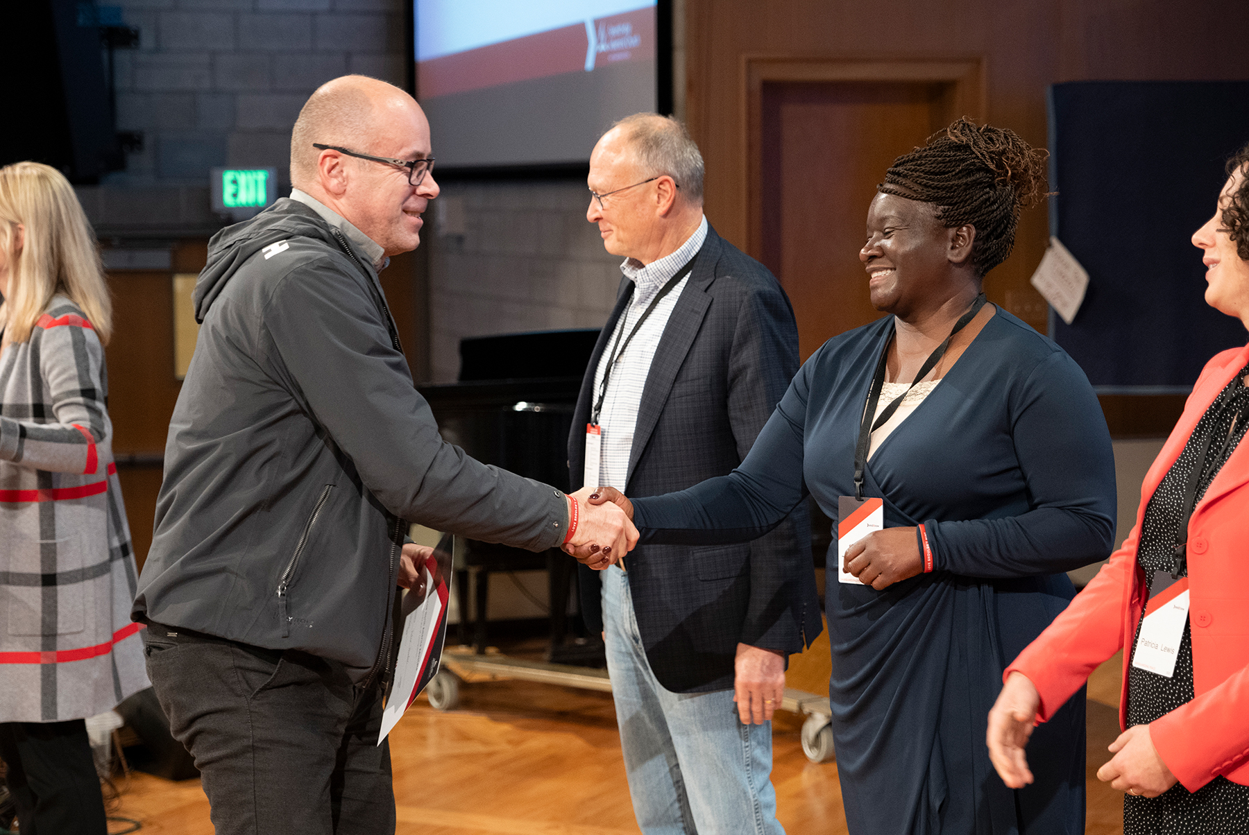 A smiling white man holding a certificate shakes the hand of a smiling black woman. Also in the picture are two white women and a white man standing in a row. It's a graduation ceremony of sorts. 