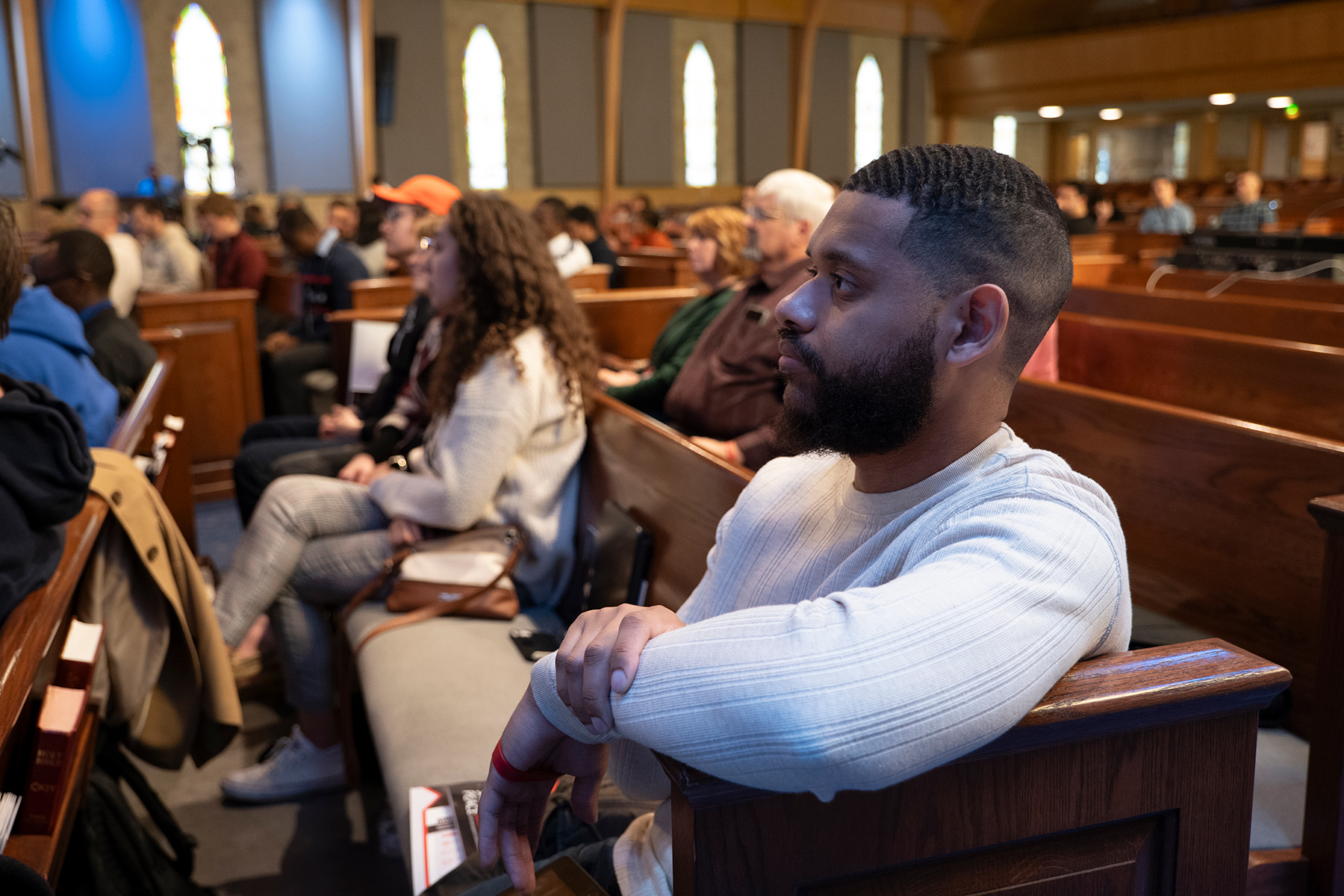 Young black man in the forefront, several people of other races and genders in the background sitting in a church.