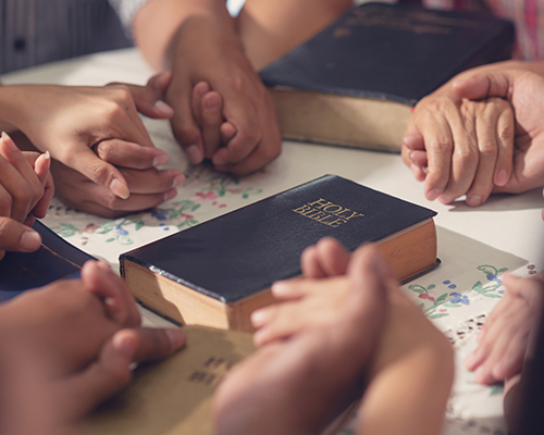 hands held in prayer around Bible