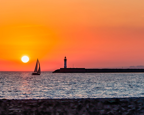 sailboat, sunset, and lighthouse stock photo