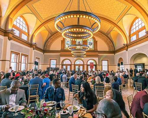 Large ballroom with many people eating a meal seated at tables