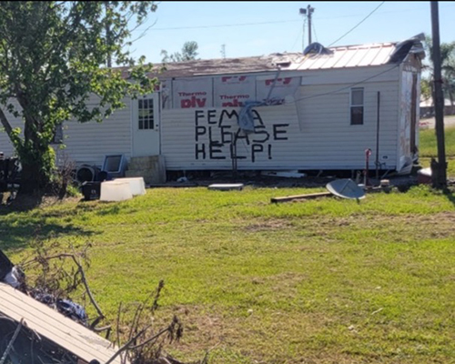 Trailer home with "FEMA please help" spray-painted on the outside wall.