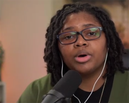 Woman with glasses speaking into a microphone