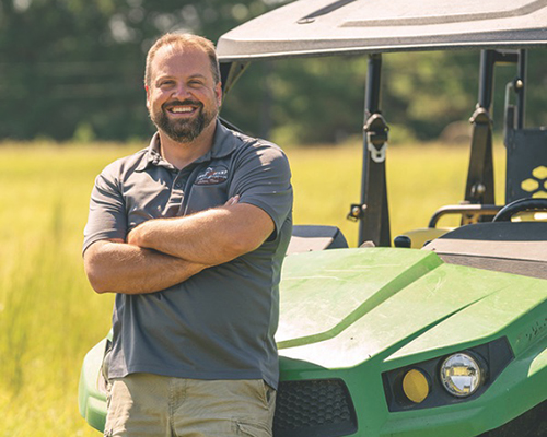 Man smiling standing in front of a golf cart in a field