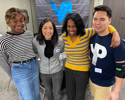 Young people standing together arm in arm smiling, three women, one man