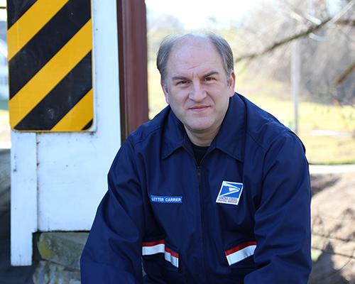 White man in US Postal Service uniform sitting outside