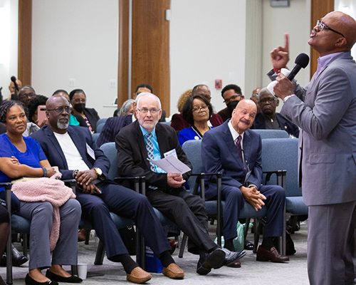 Black man speaking to a diverse crowd of men and women