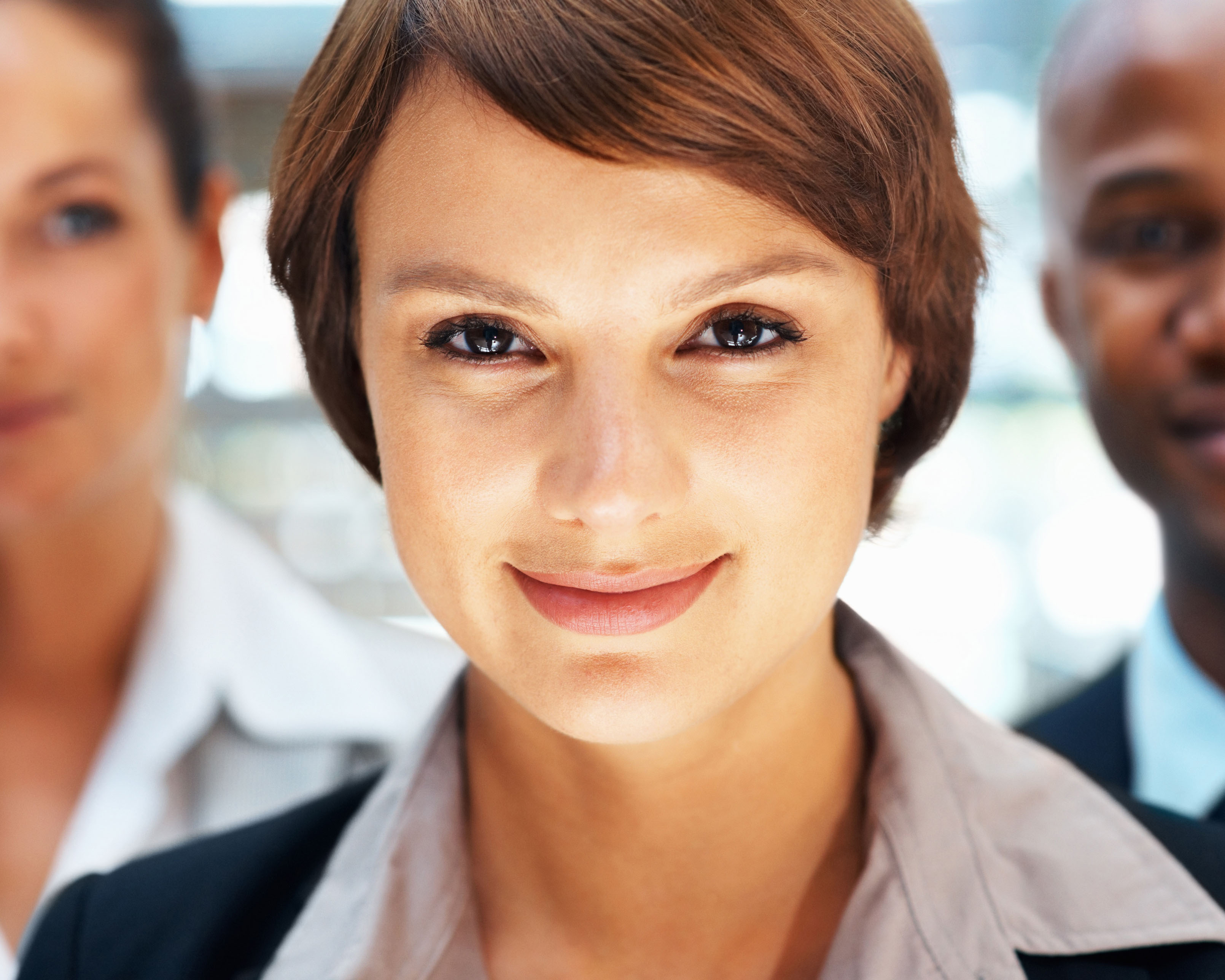 Woman in business suit looking towards camera with two coworkers by her side.