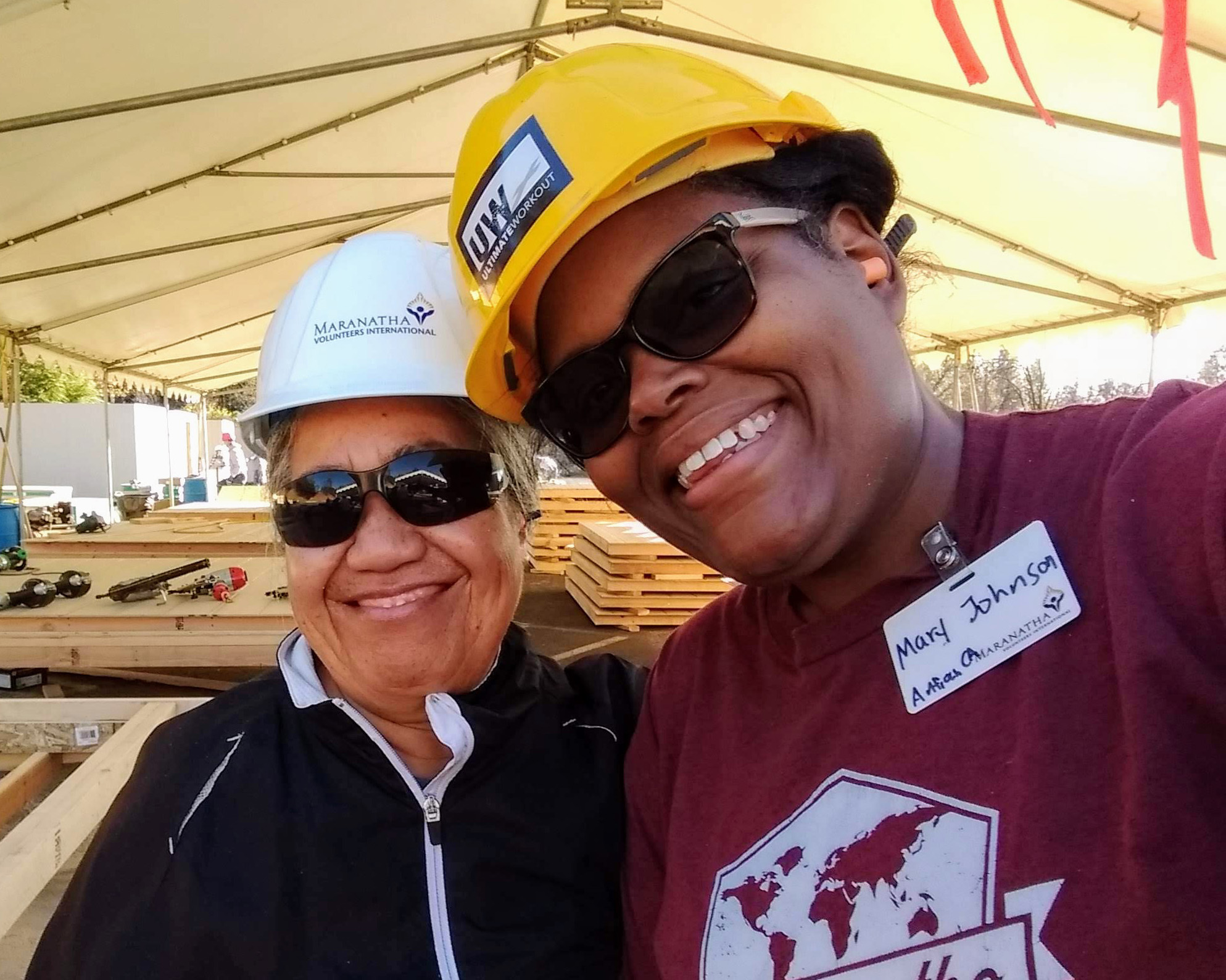 Two women in construction hats smiling and looking towards the camera.
