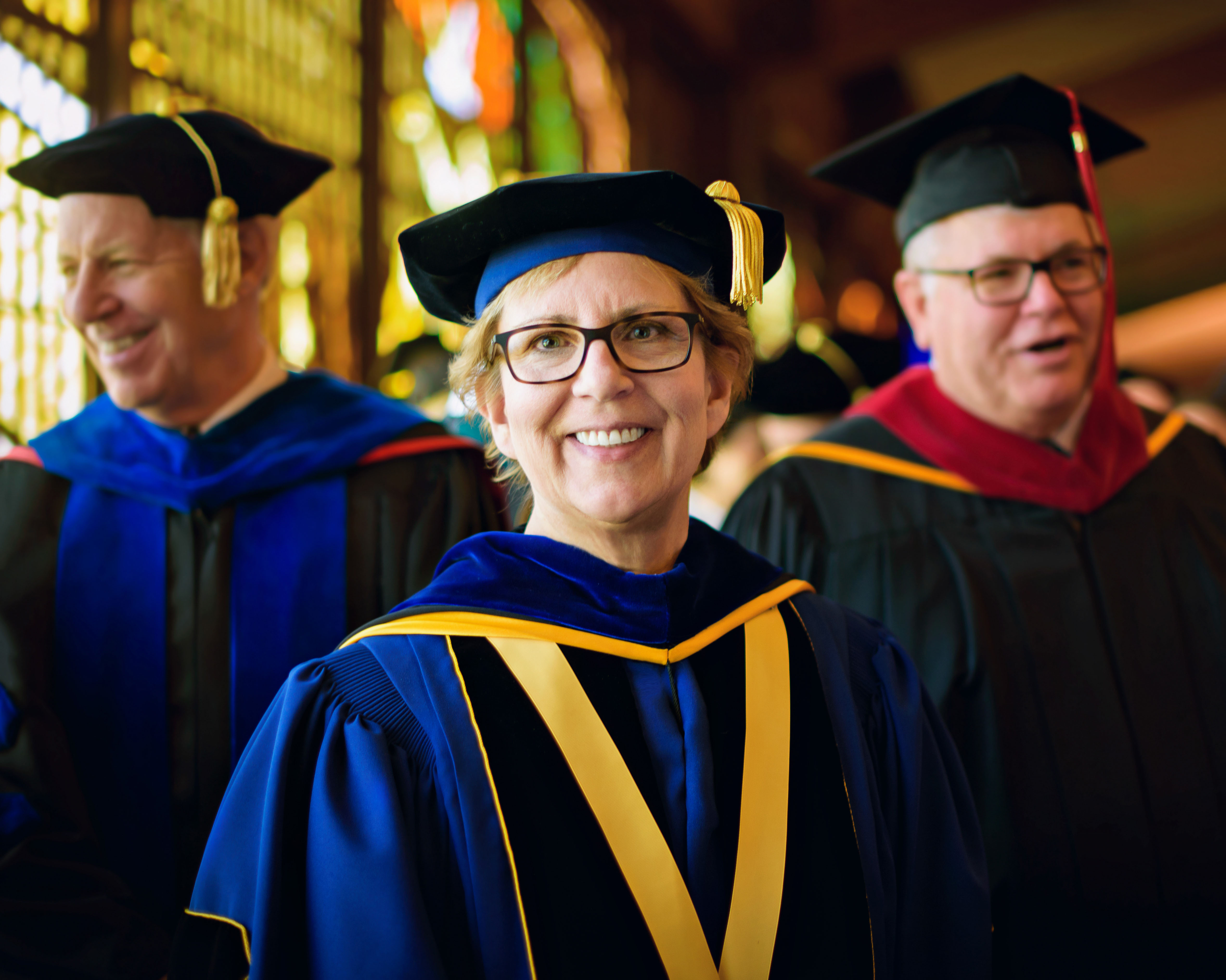 Woman in graduation attire smiling next to two other people in graduation attire. 