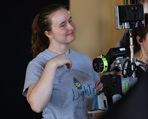 A smiling young woman looks through a video camera