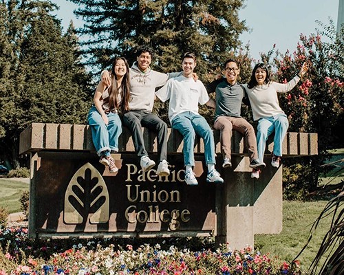 A small group of students sitting on a sign reading "Pacific Union College"