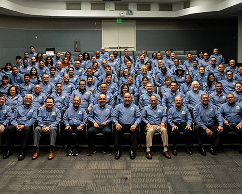 Men and women in an auditorium wearing matching blue dress shirts