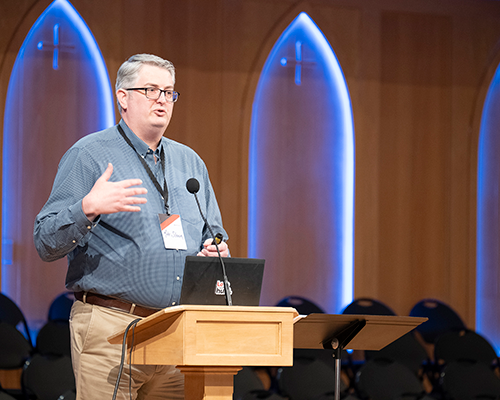 White man standing at a podium, speaking.