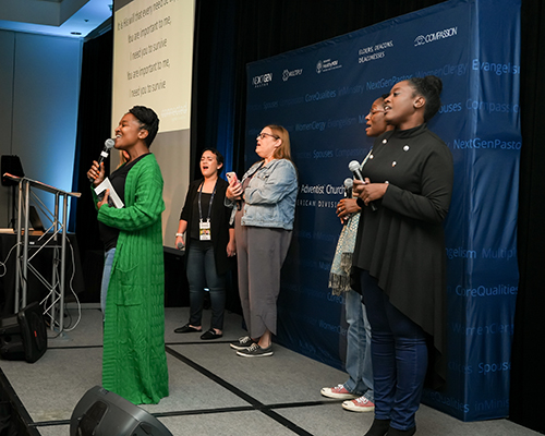 Women of all ethnicities singing together on a stage. 