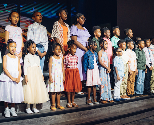 Several black children singing on stage in a choir