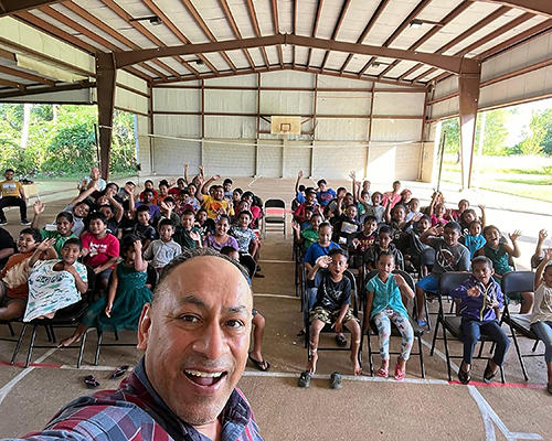 Hispanic man standing in front of children in uniform taking a selfie