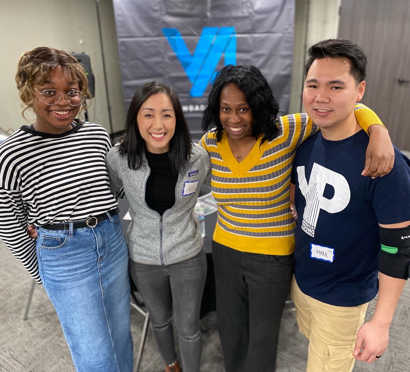 Young man and three young women standing together arm in arm and smiling