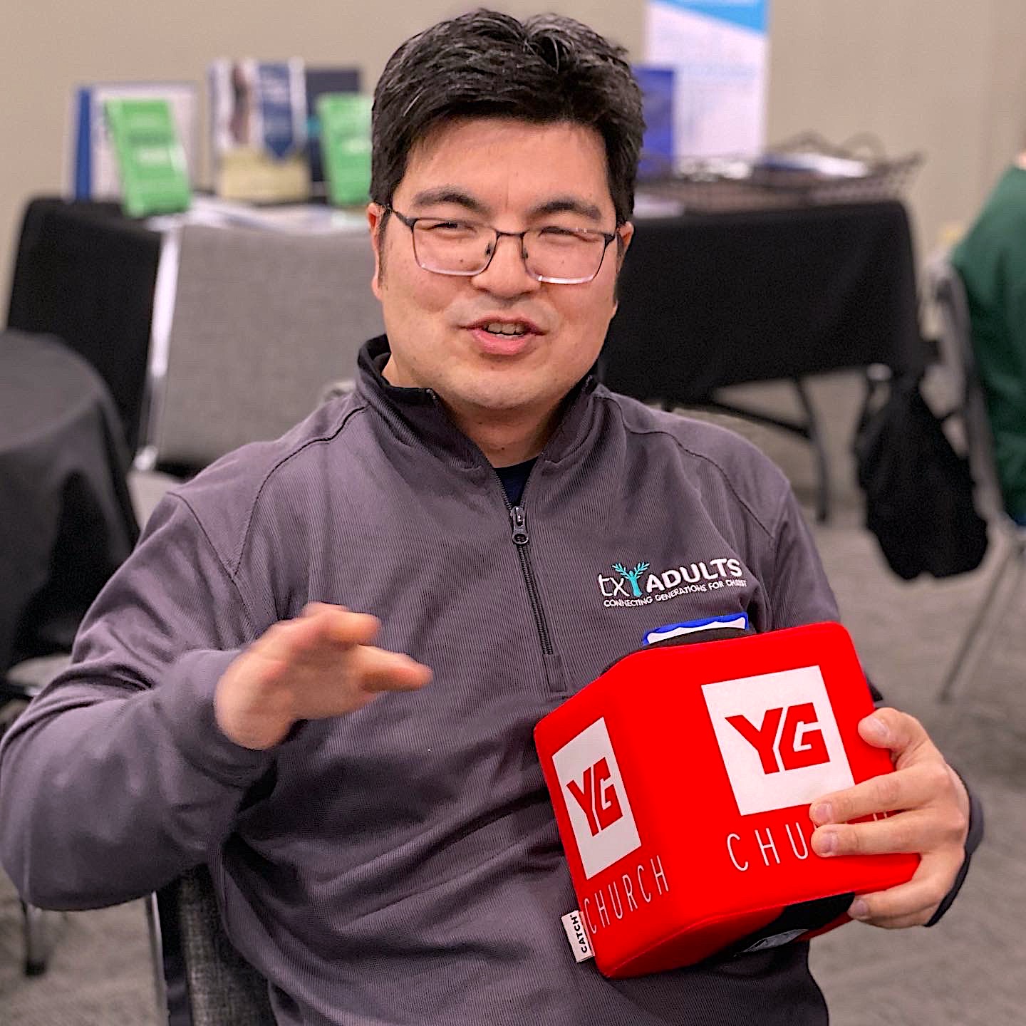 Asian man seated with a plush red square reading "YG Church"