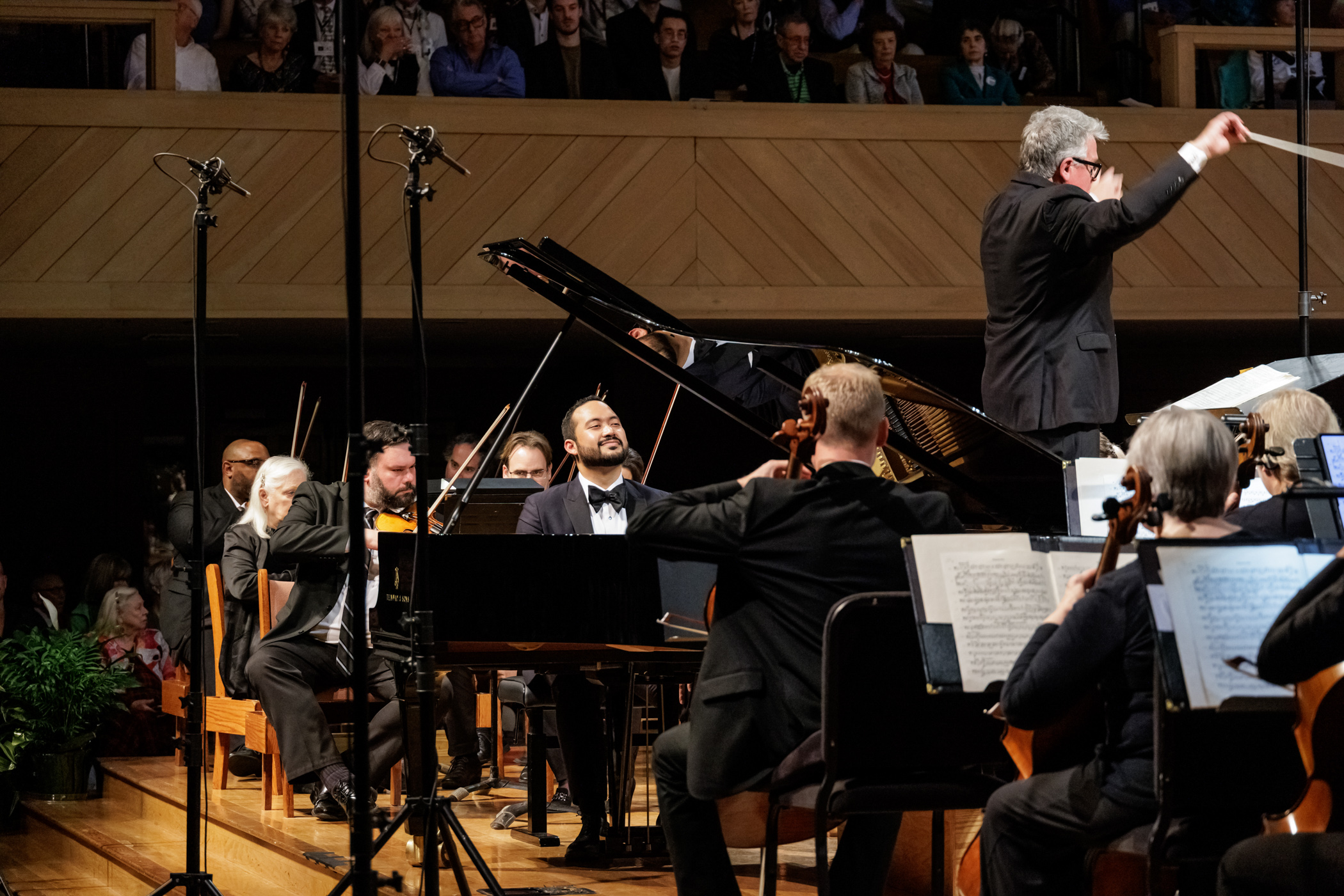 Jonathan Mamora plays the grand piano as part of an orchestra un front of a large crowd.