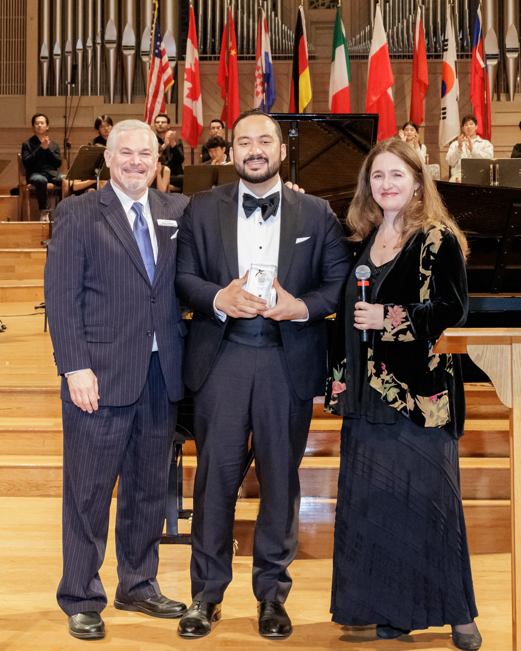 Pianist Jonathan Mamora holds his award standing with supporters.