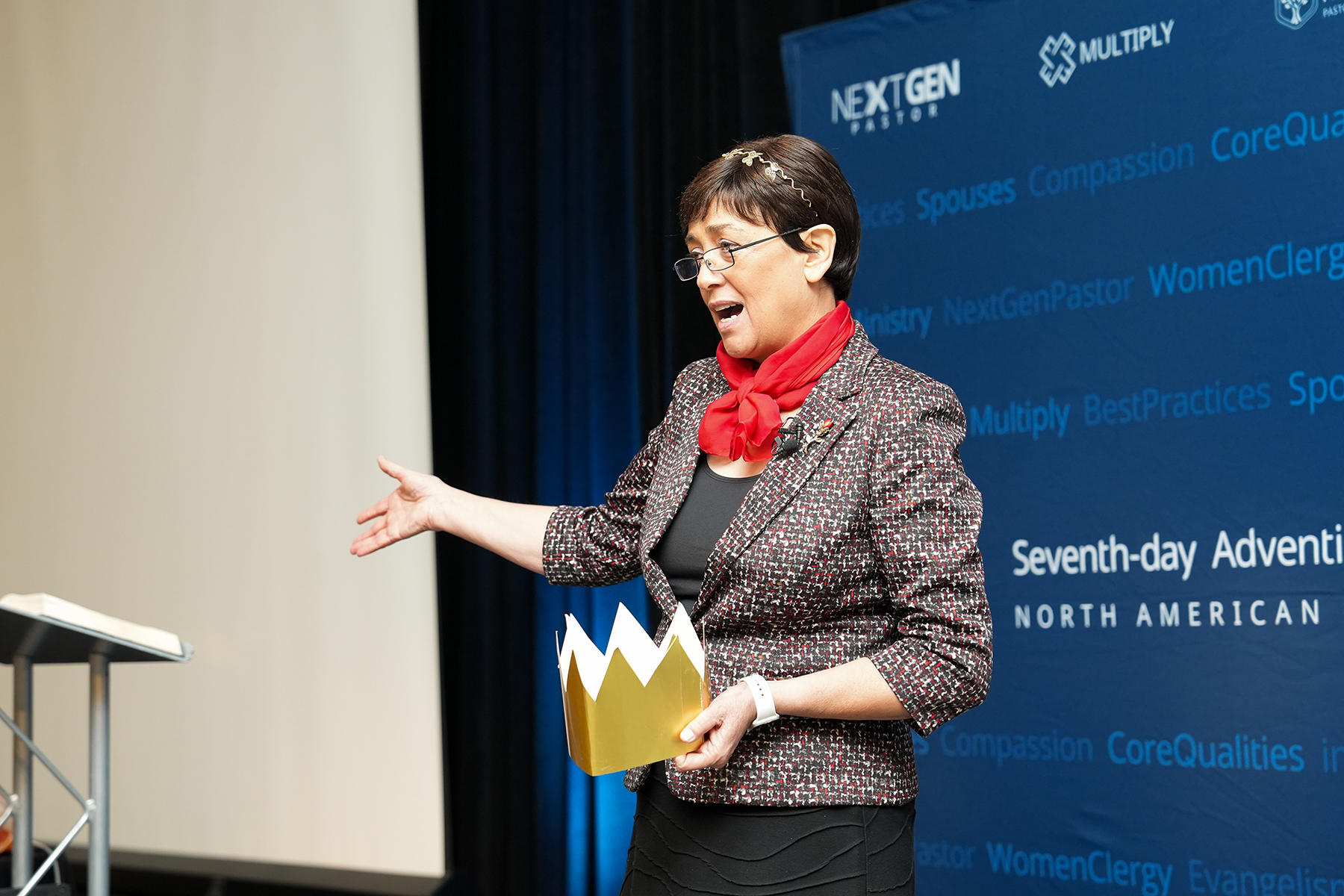 A Hispanic woman holds a golden paper crown and is speaking to an unseen crowd.