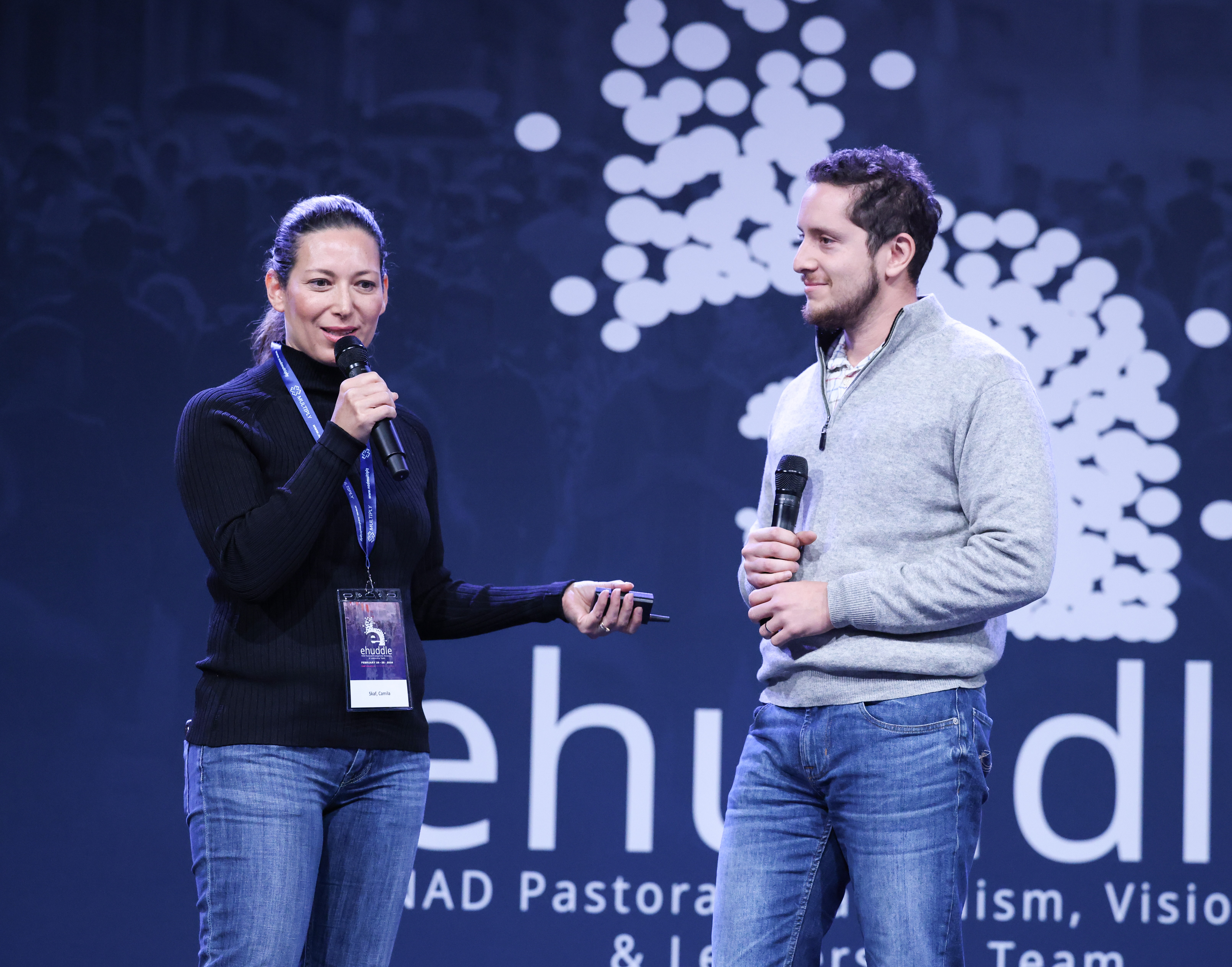 A white woman and white man presenting on stage at a conference. The woman is holding the mic.