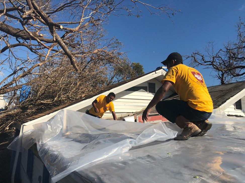 ACS volunteers lay a tarp over an exposed home. 