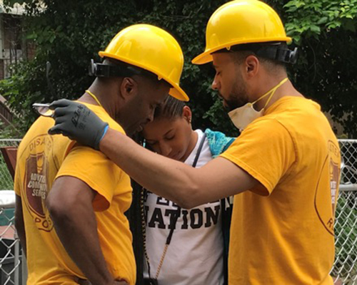 Derrick Lea, director of ACS DR (L) and David Franklin, pastor of Miracle City Seventh-day Adventist Church (R) pray with Dionne, a local resident whose home was significantly affected by flooding over Memorial Day weekend. Photo courtesy of ACS