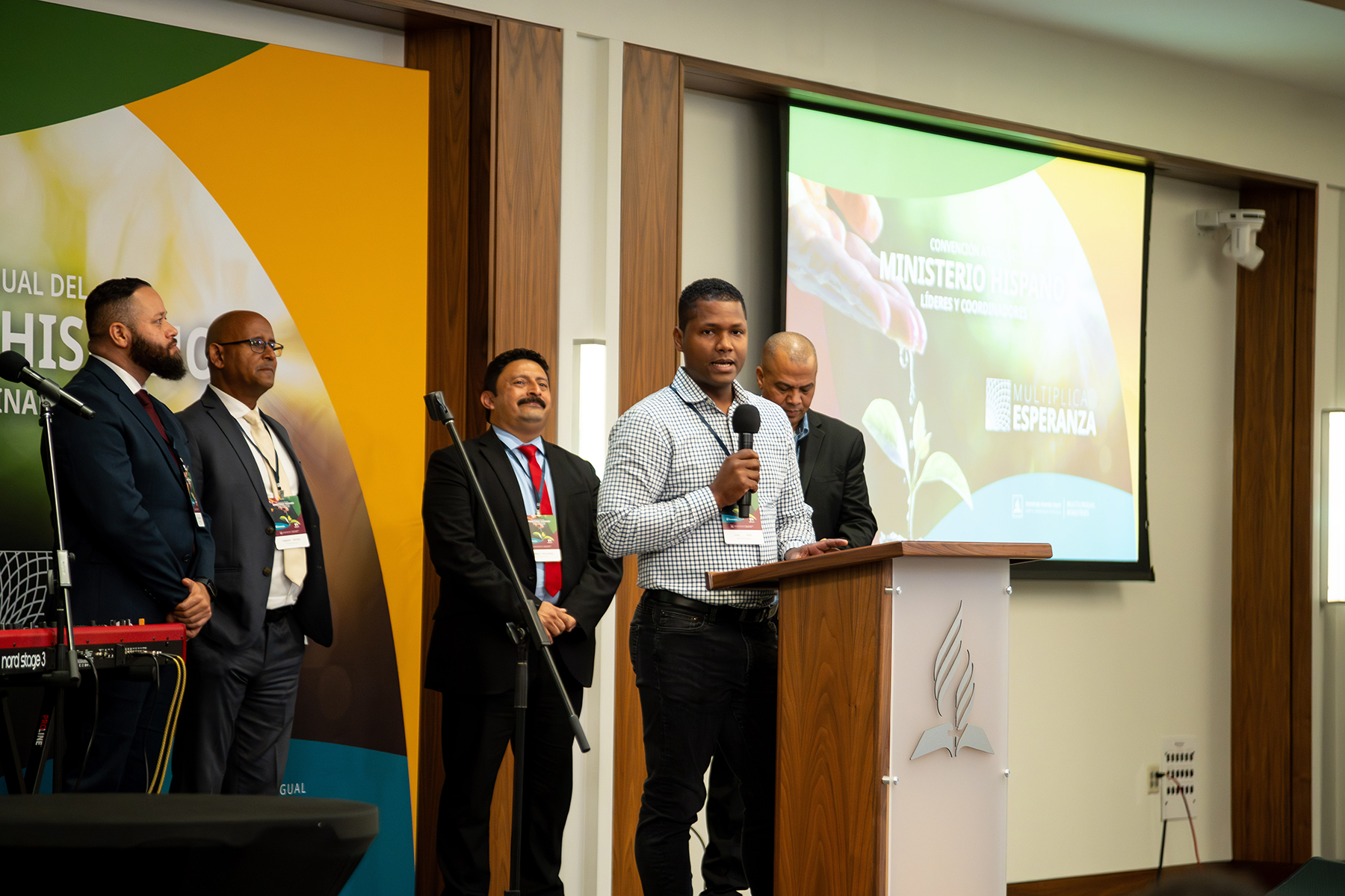 Men standing on a podium, one standing behind a microphone speaking