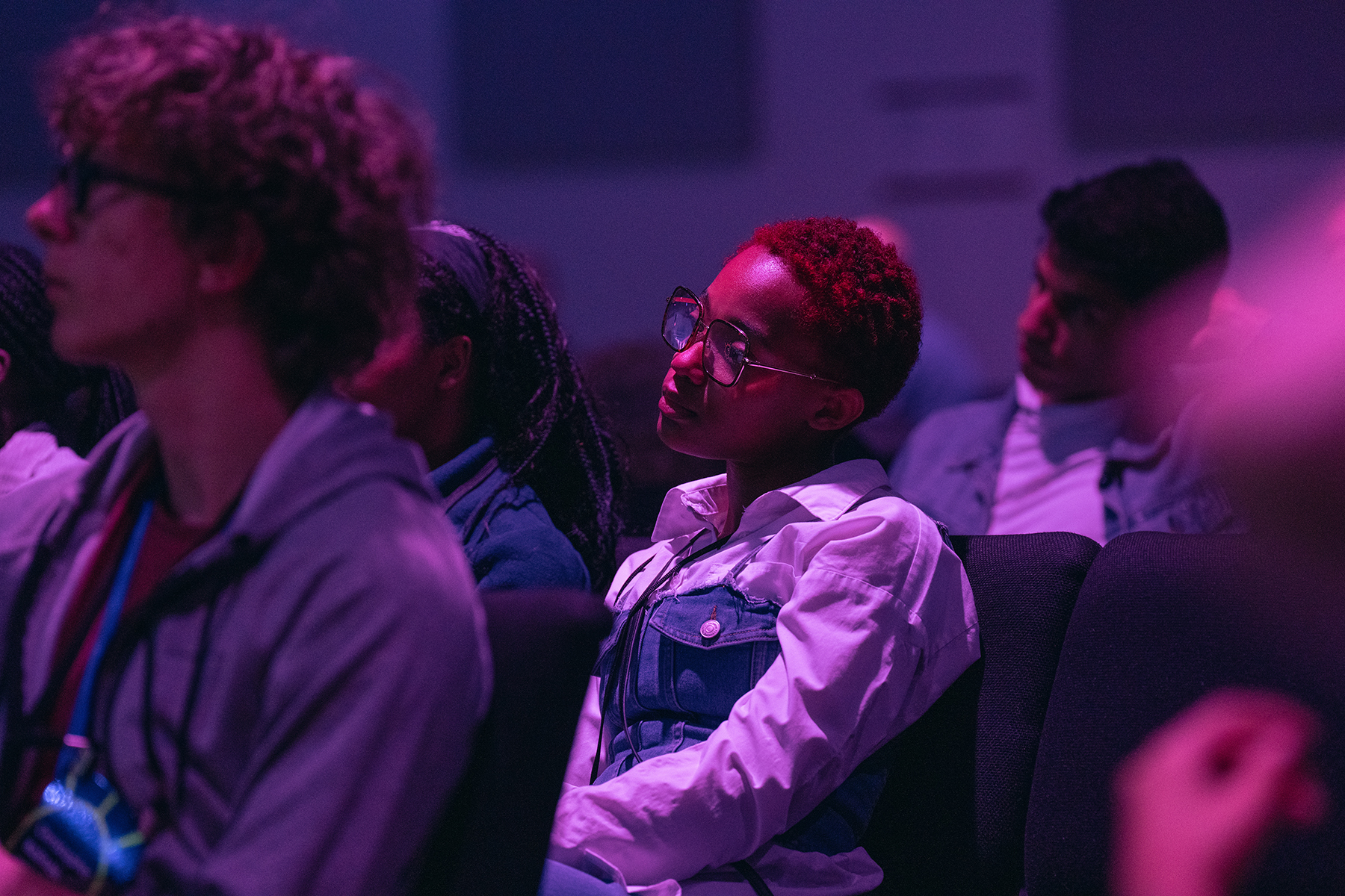 A photo of people watching an unseen stage. Central person is a black woman with red hair.