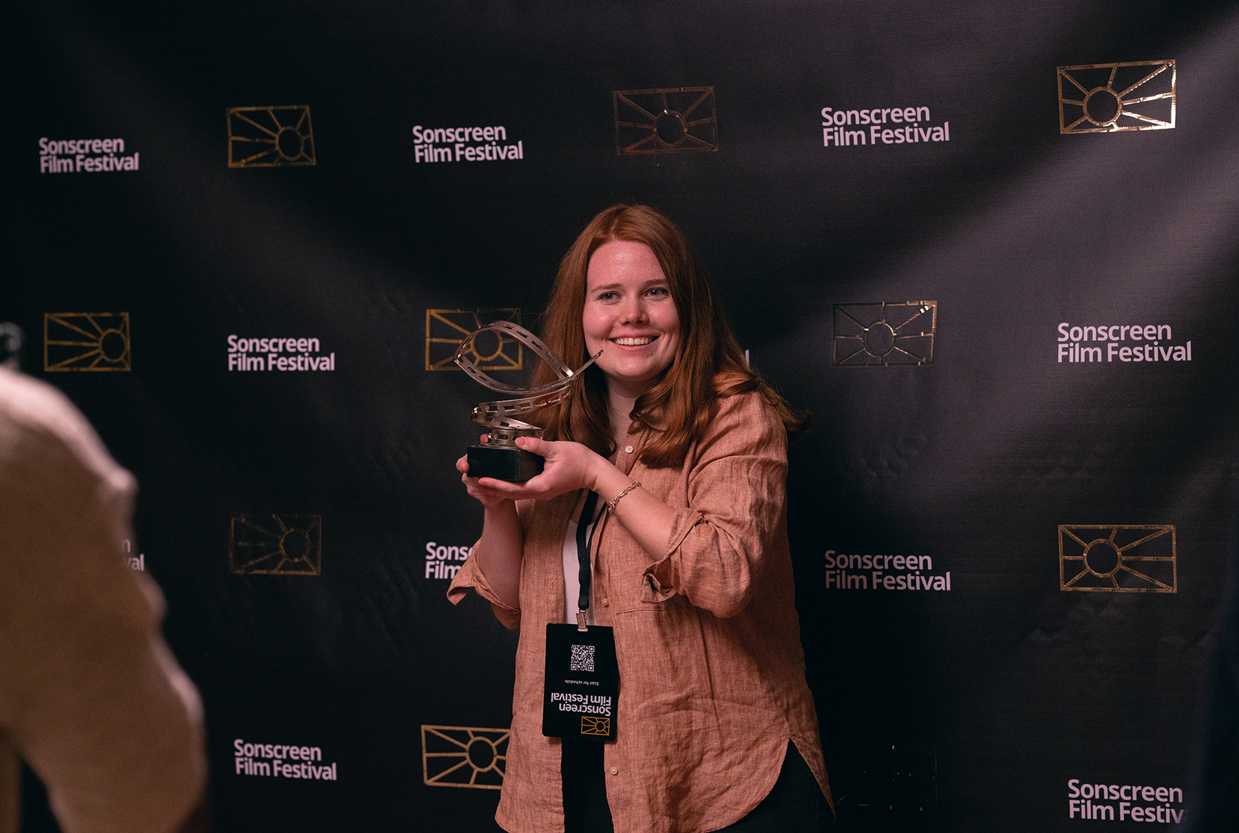 A young woman holds up an award in front of a media wall.