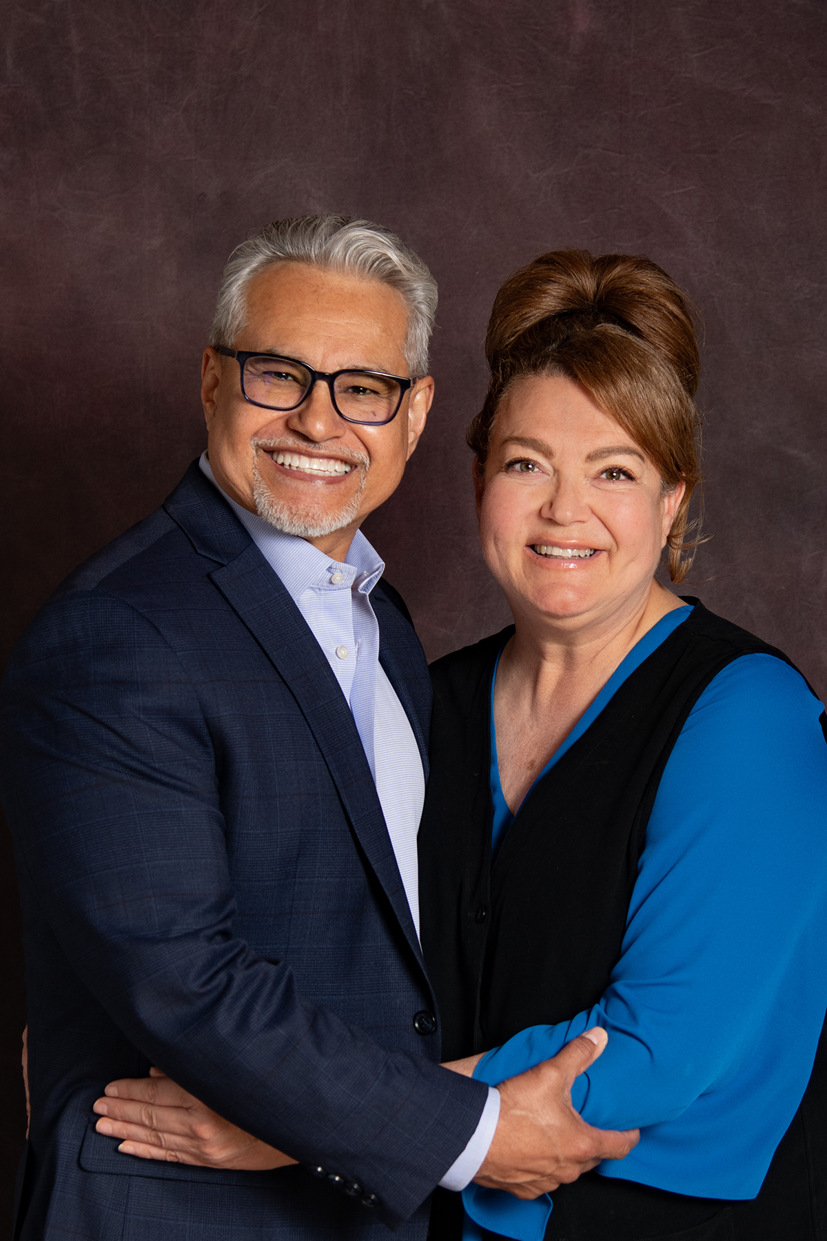 A smiling Hispanic couple pose for a formal photo with arms around each other