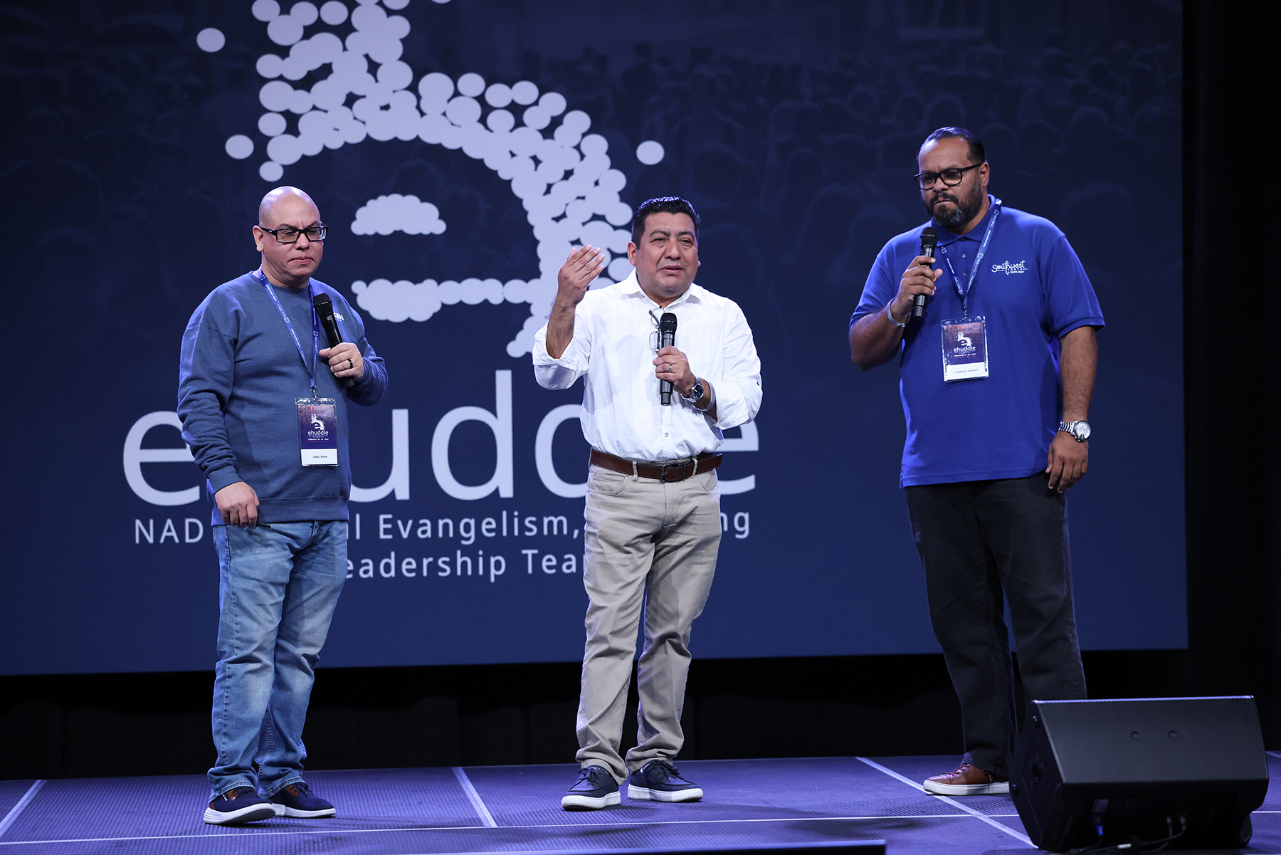 Three Hispanic men stand on a stage together.