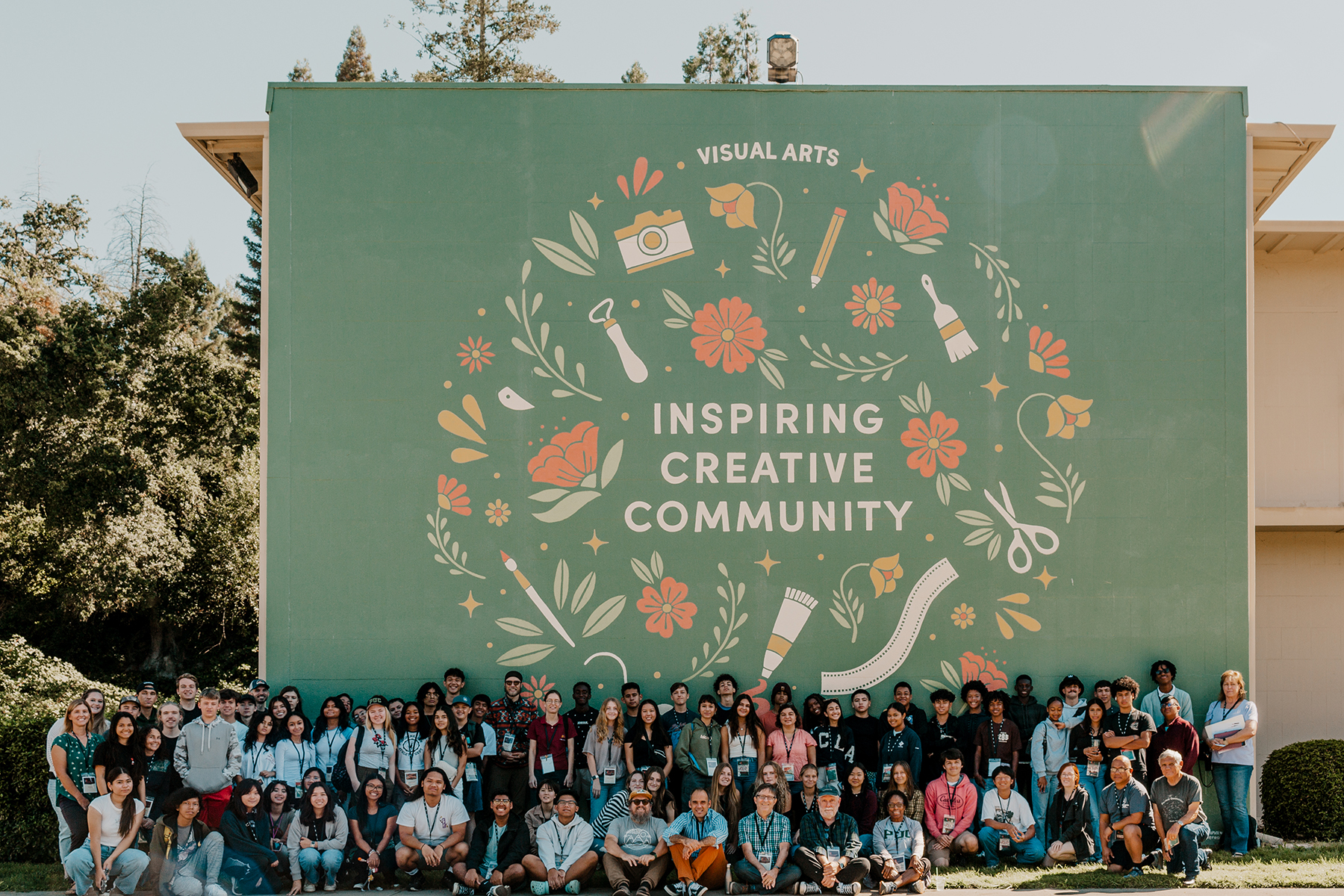 Several students stand in front of a sign reading "Visual Arts: Inspiring Creative Community"