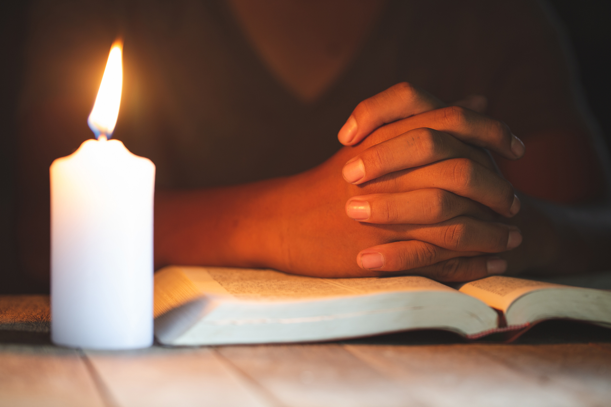 stock photo of person praying with bible in candle light