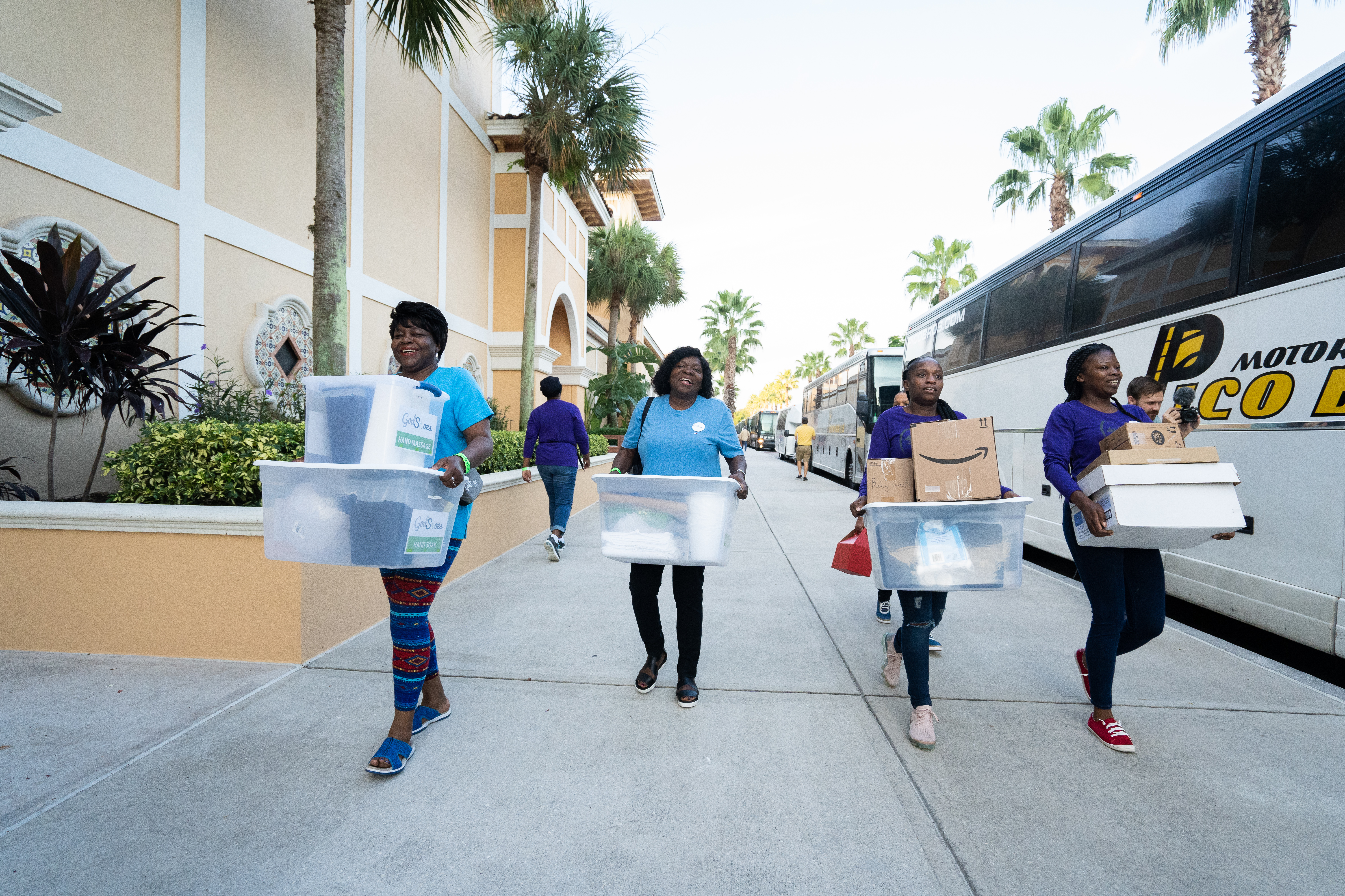 Four women carry supplies to be loaded onto a bus and donated during God in Shoes community service day.