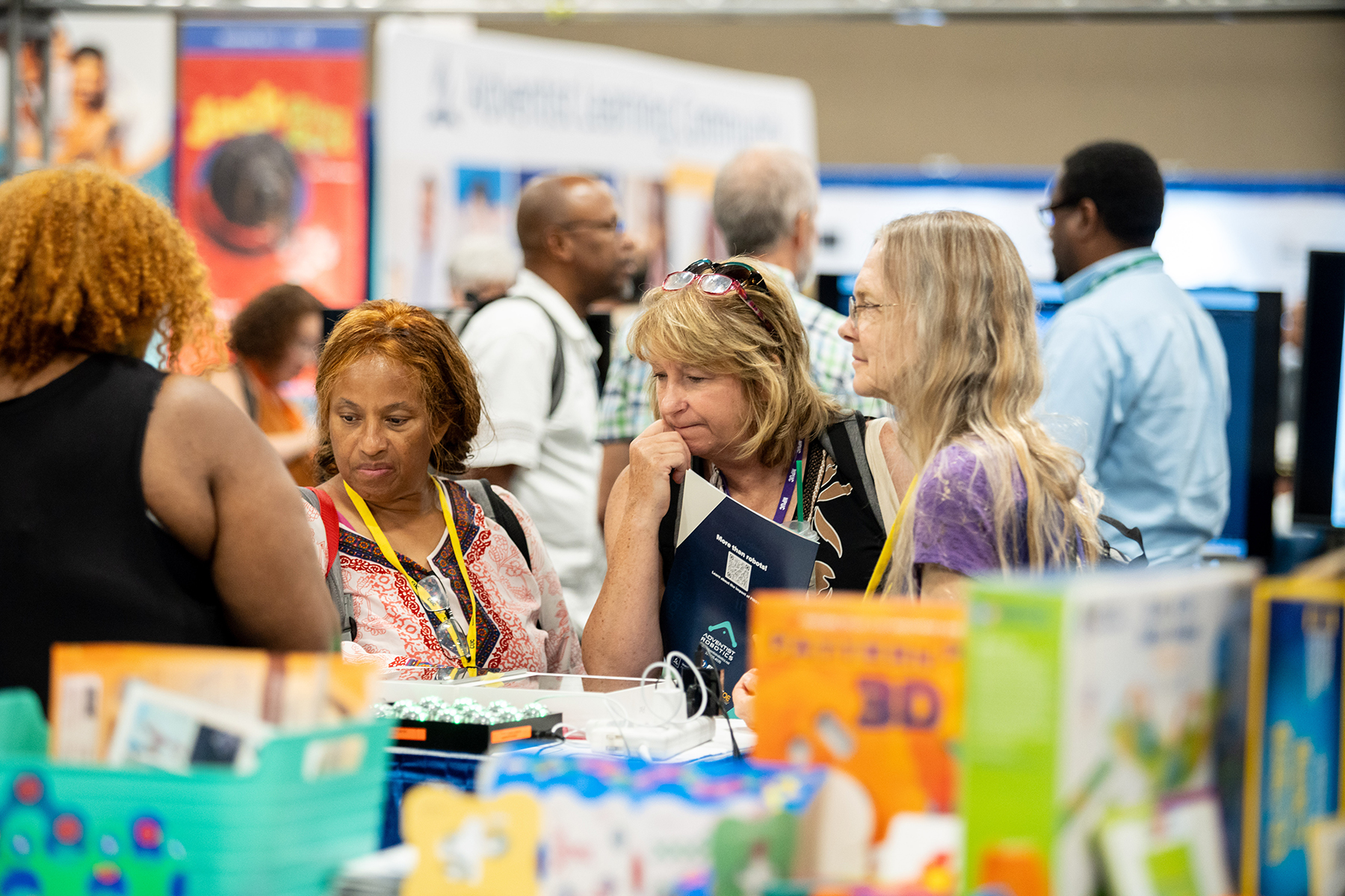 Three women look at a blurred-out table of science toys.