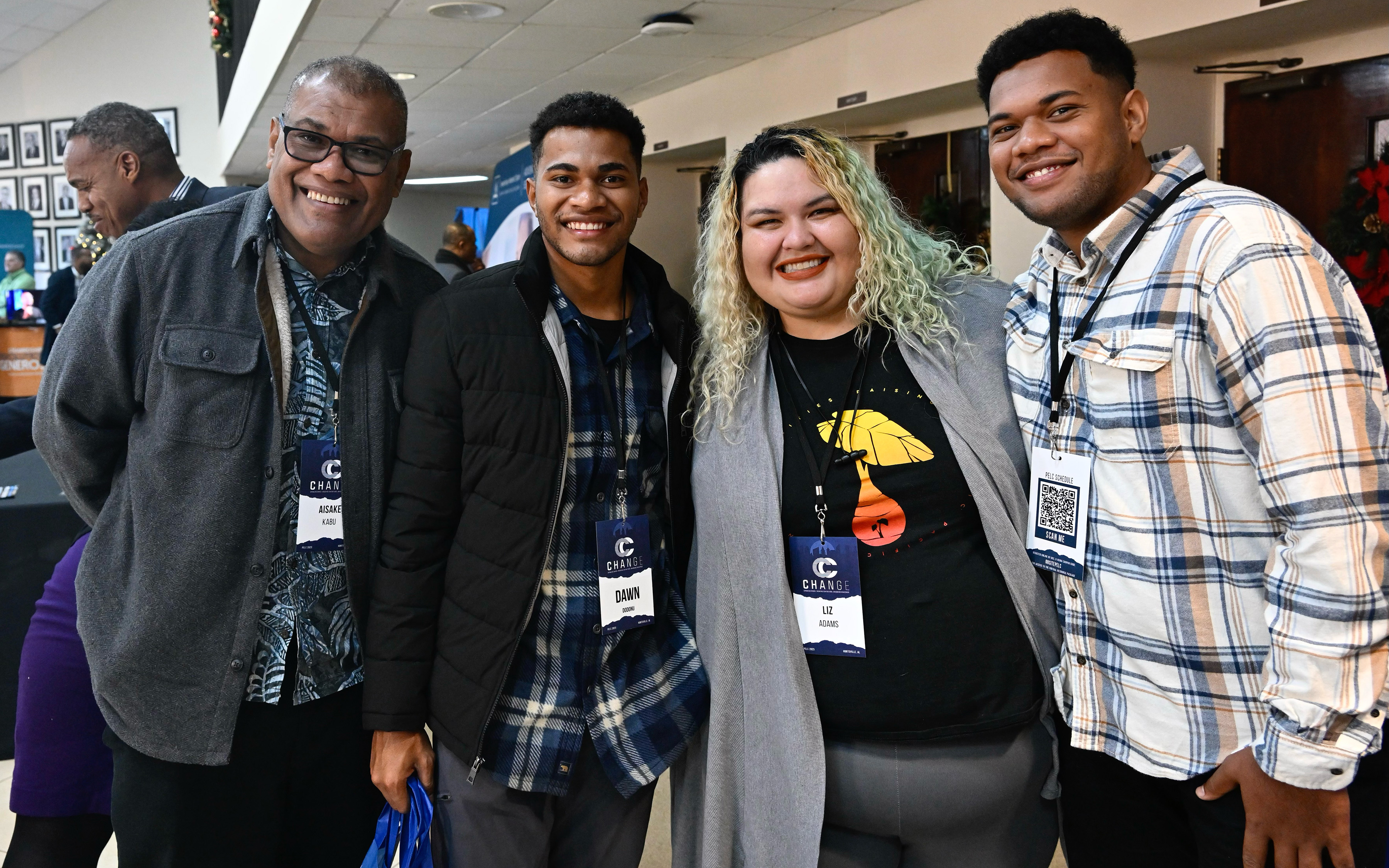 Left to right: Two brown men, one Hispanic woman, and one brown man in the hallway of a church being used for a conference. Another man is just behind them. 