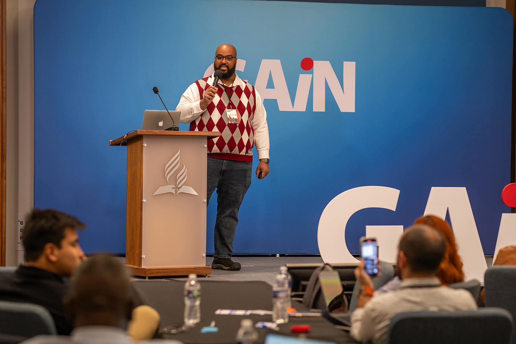 Black man stands behind a podium speaking to people