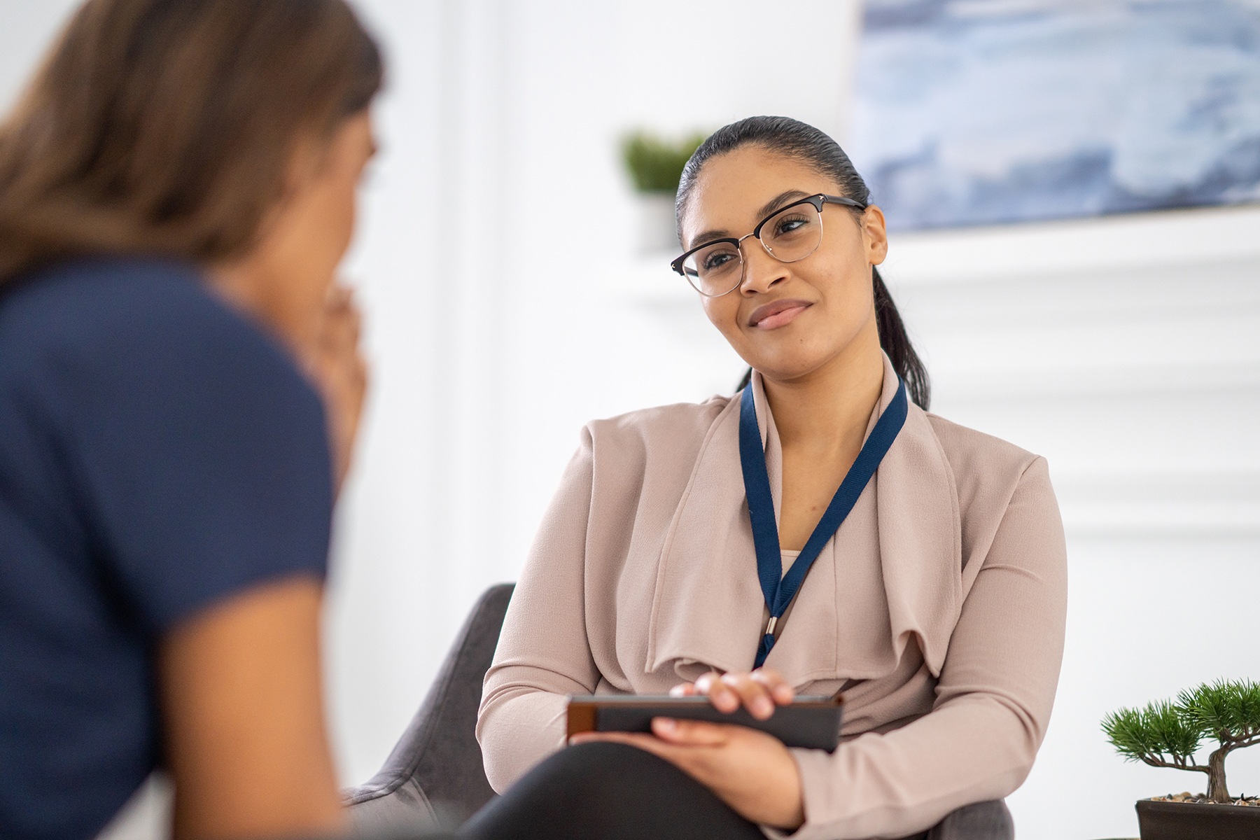 School counsellor with glasses and holding a clipboard sits across from a student. Counsellor is in focus. Student is blurry.