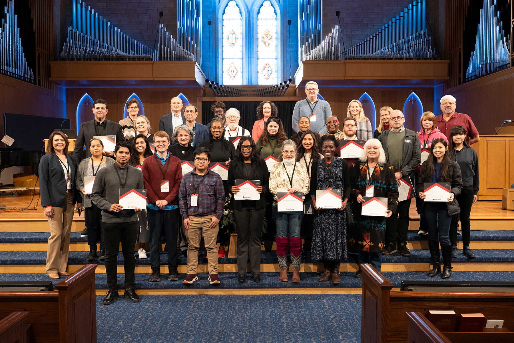 A group of individuals of different genders, ages, and races standing on a stage in a church. 