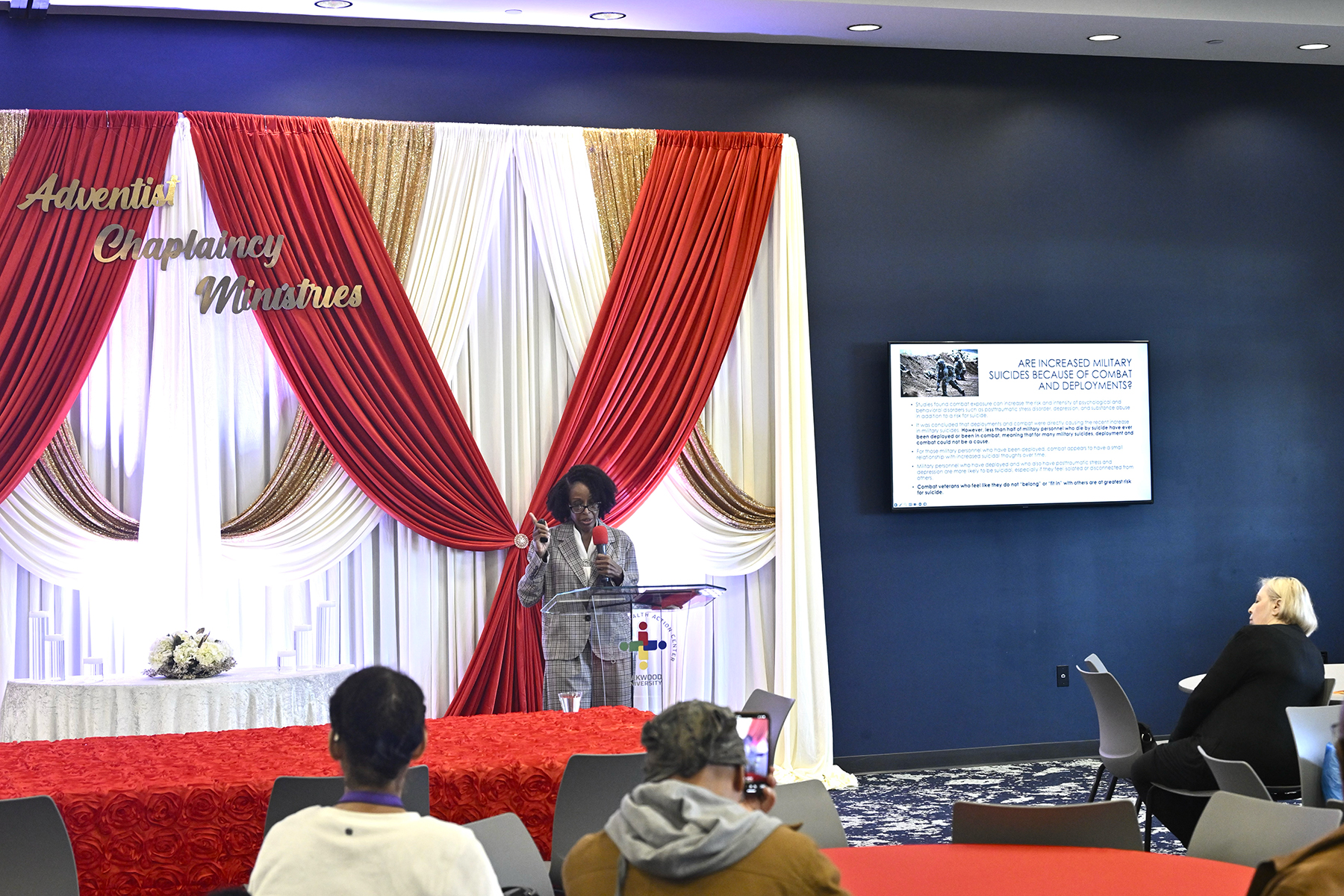 A Black woman is standing in front of a red background reading Adventist Chaplaincy Ministries.