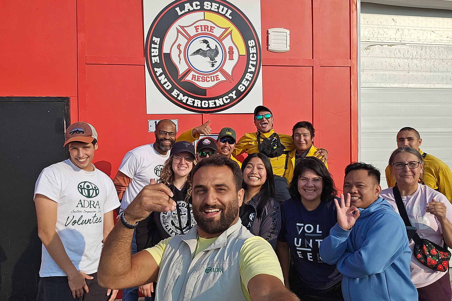 A diverse group of smiling people stand in front of a sign reading "Lac Seul Fire and Emergency Services."