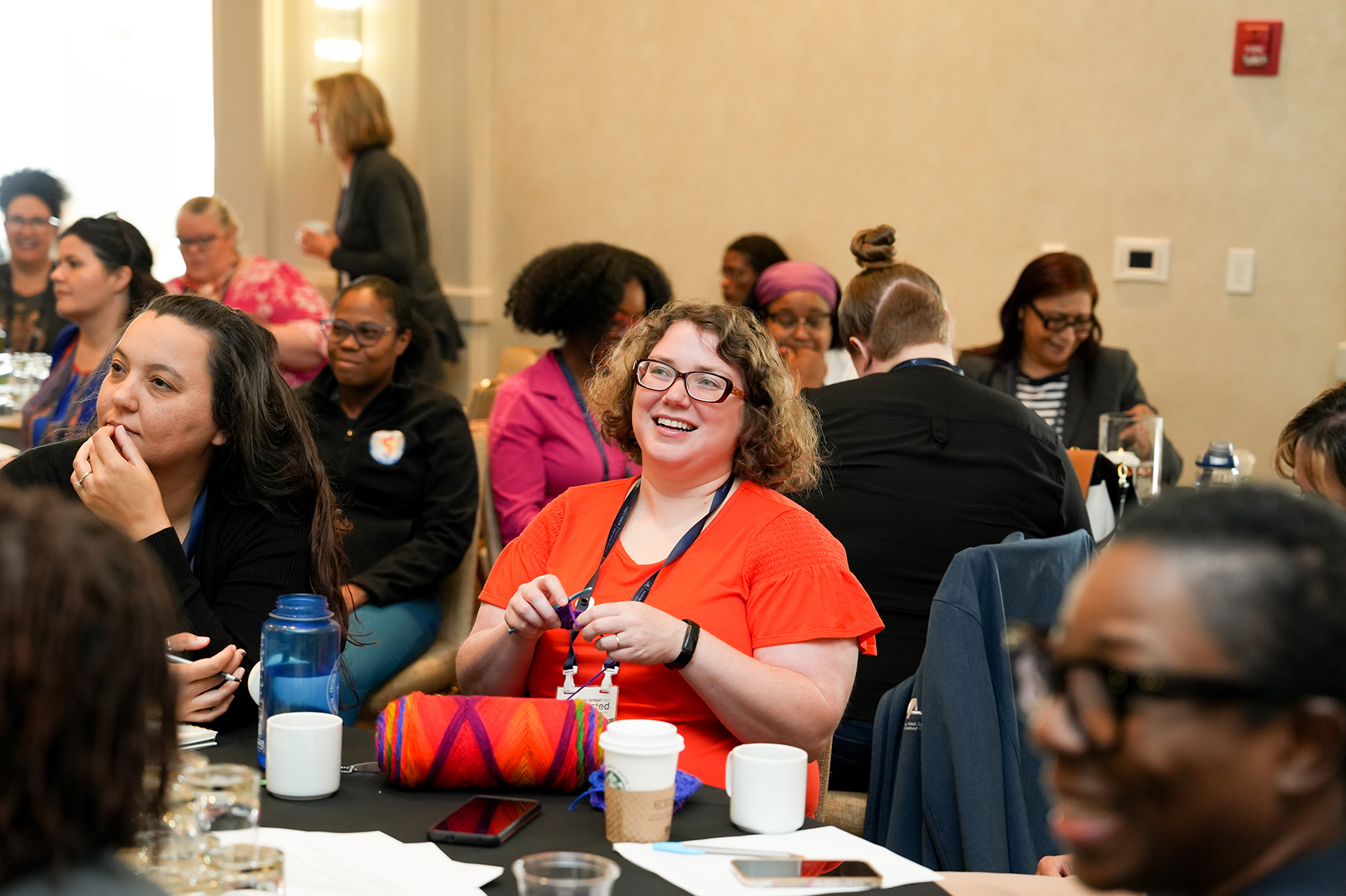 Smiling white woman in the midst of a room of women sitting at tables. 