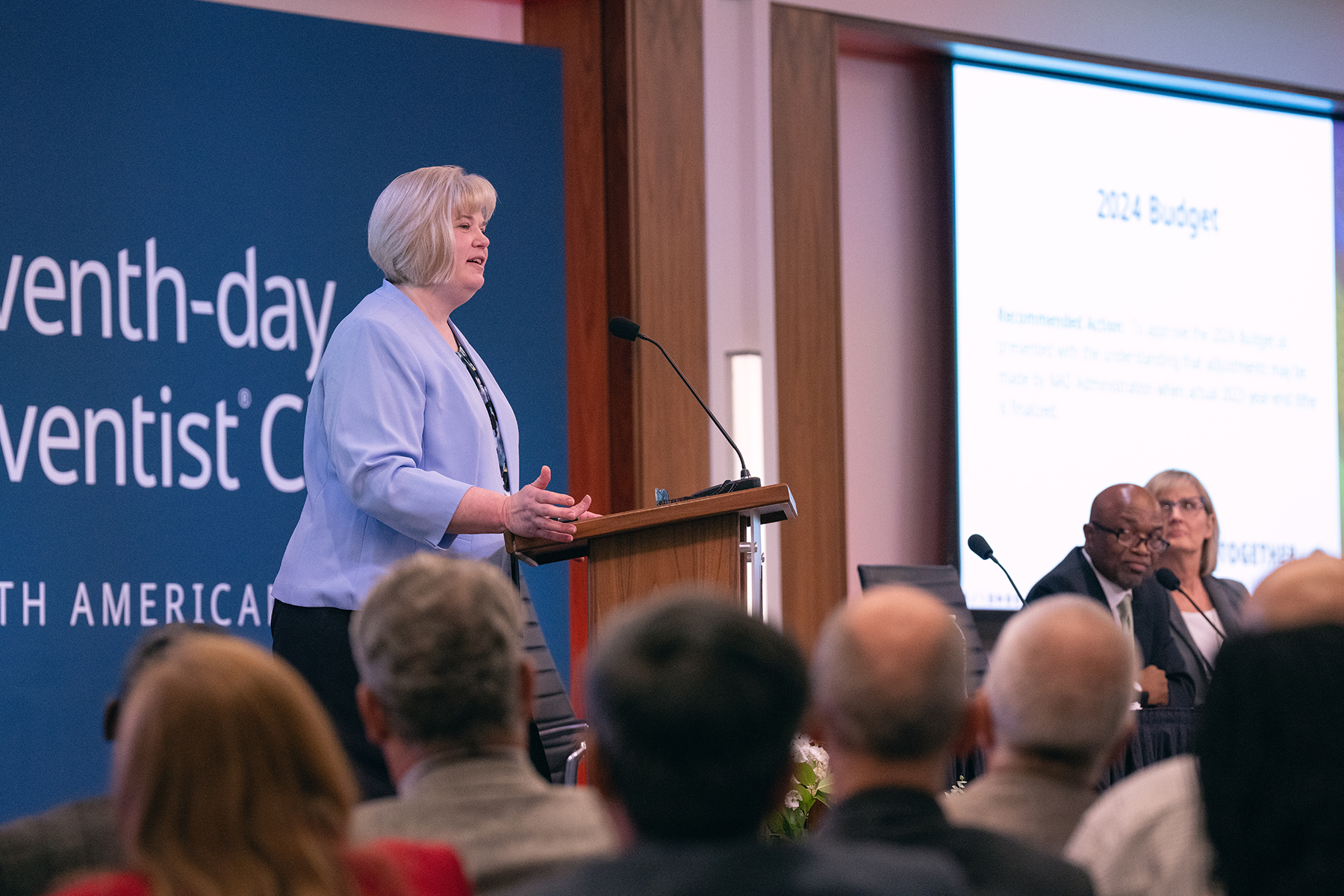 Smiling white woman speaking to a crowd from behind a podium.