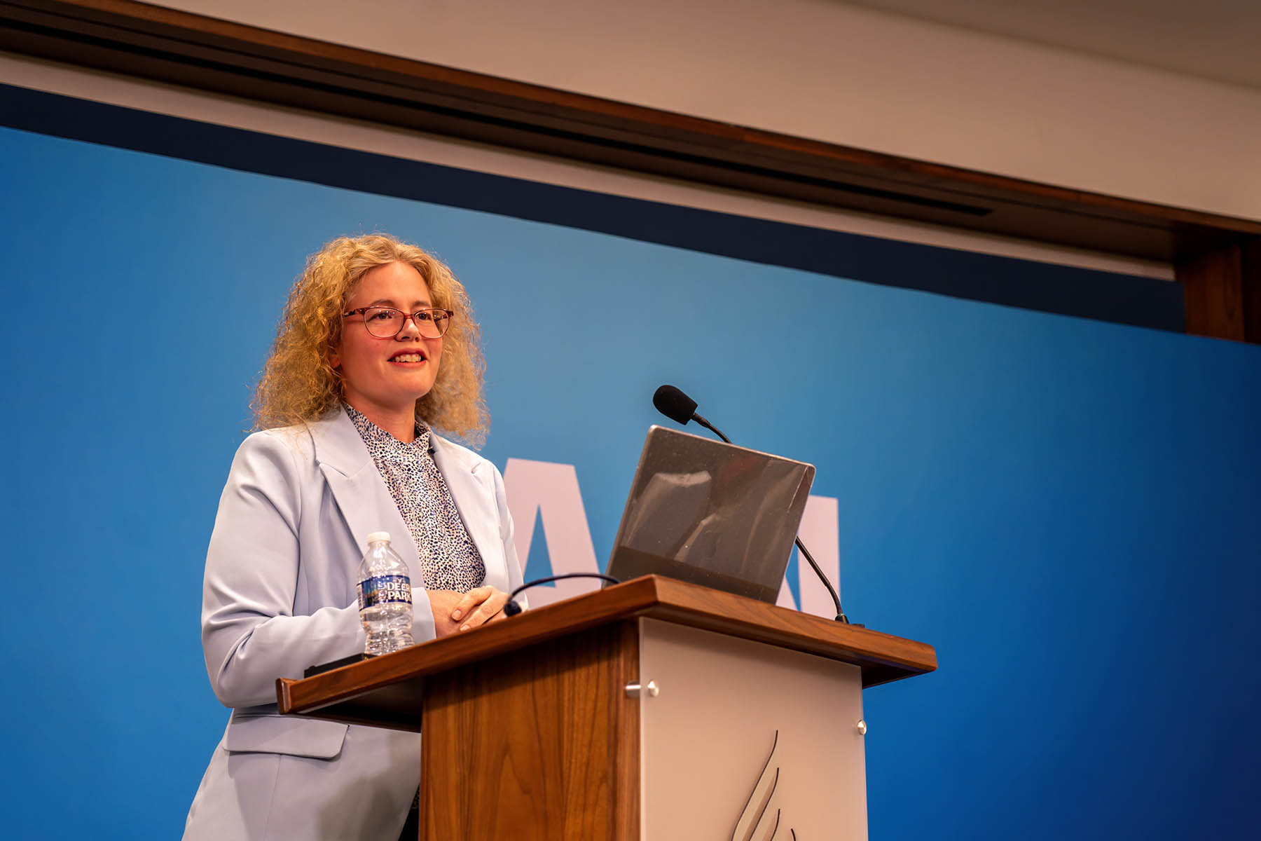 A white lady stands behind a podium smiling