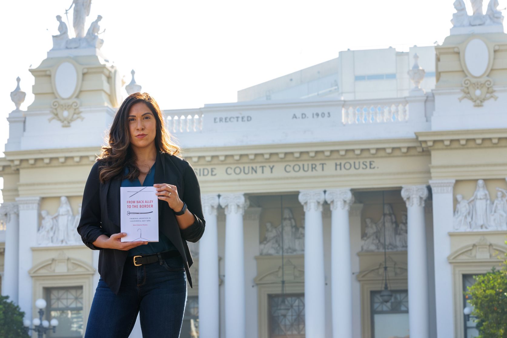 Dr. Alicia Gutierrez-Romine poses with her book in front of the historic Riverside County Courthouse. Photo by Natan Vigna